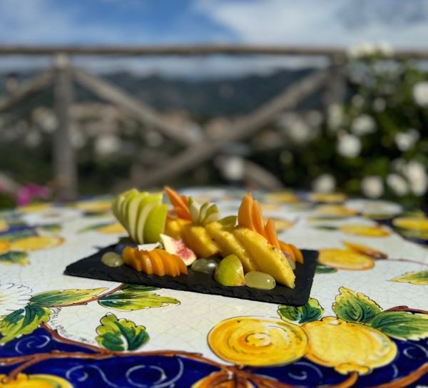 Frutta fresca servita su tavolo decorato in ceramica durante una colazione all’aperto in Costiera Amalfitana